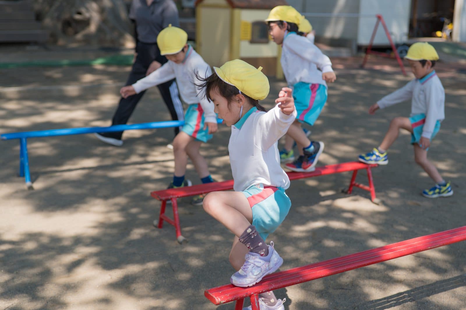 運動ローテーションで、園庭の平均台をバランスをとりながらわたる子どもたち